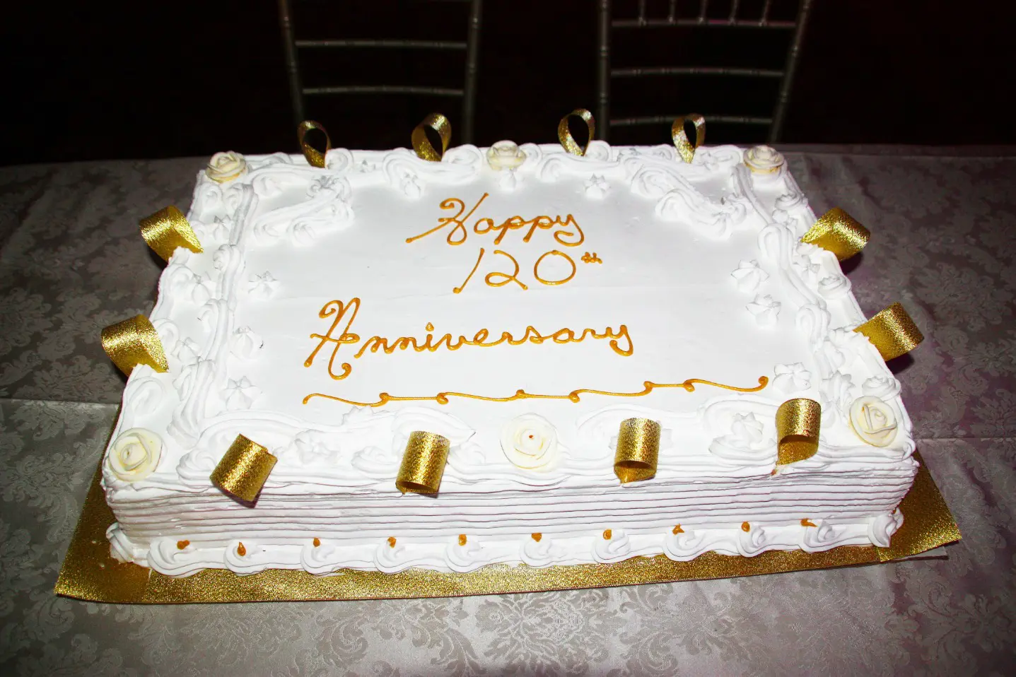 A white sheet cake with gold lettering and candles.