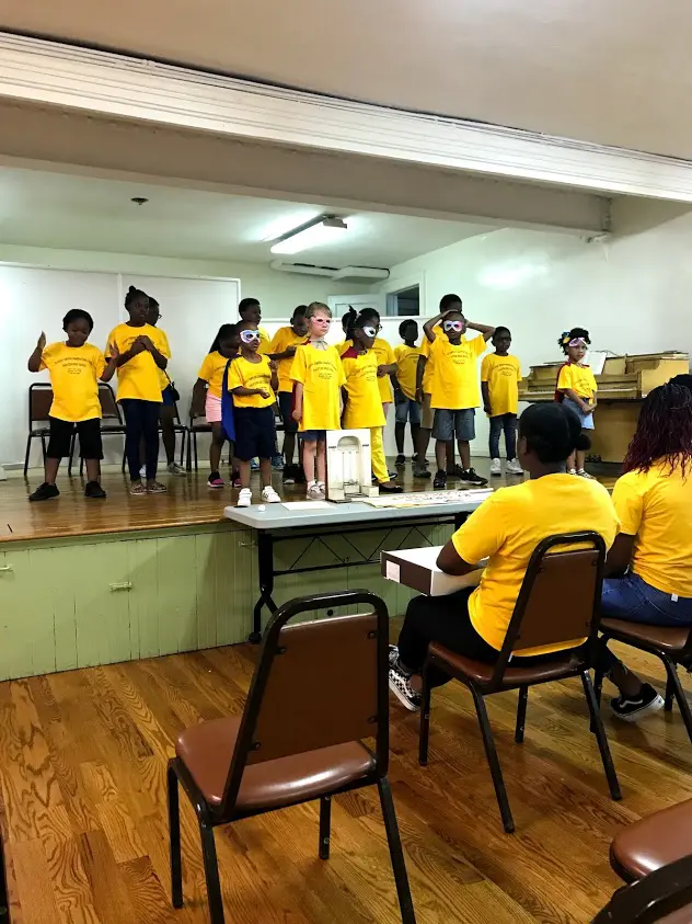 A group of children standing on stage in front of a mirror.